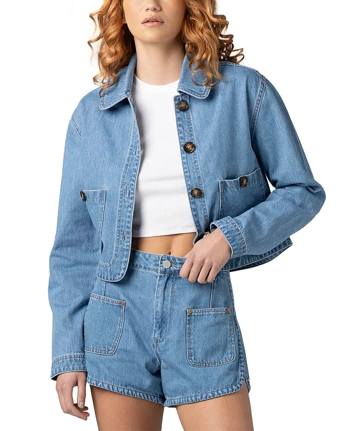 Woman wearing a cropped denim jacket with button front and front pockets styled with matching denim shorts