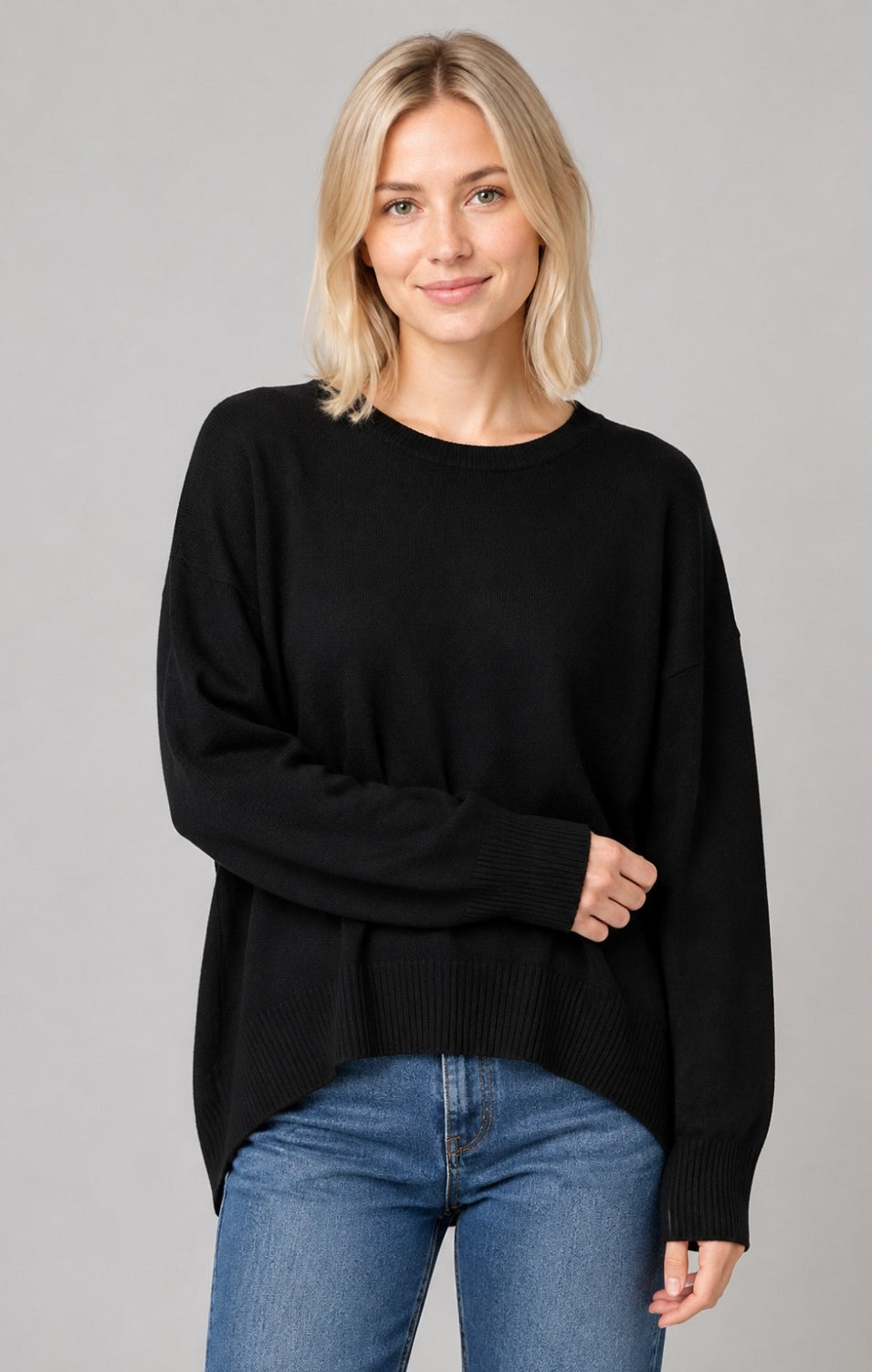 Woman wearing a relaxed crewneck sweater with dropped shoulders, ribbed trim, side slits, and a high-low hem.