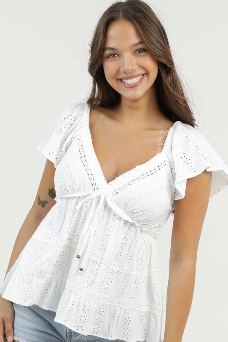 Eyelet blouse with v-neckline, flutter sleeves, and tiered silhouette styled with denim