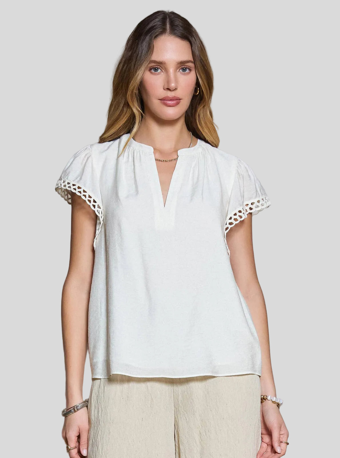 Short sleeve blouse with split neckline and decorative trim on sleeves, worn with relaxed pants.
