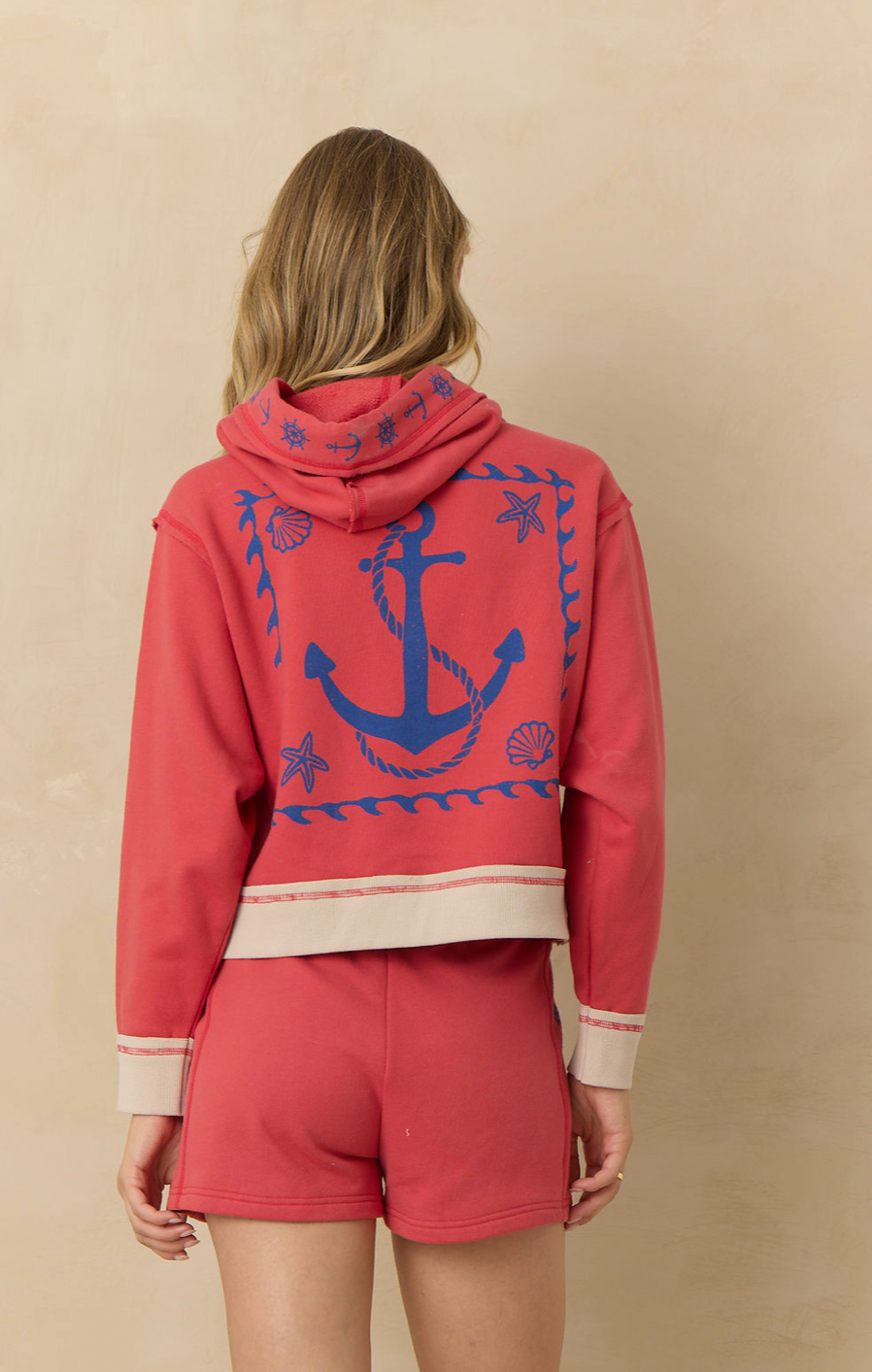 Cropped coral hoodie with nautical anchor graphic on the back, contrast trim, quarter zip neckline, and relaxed fit paired with matching lounge shorts.