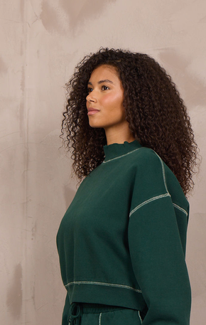 Woman wearing a mockneck pullover with contrast stitching.