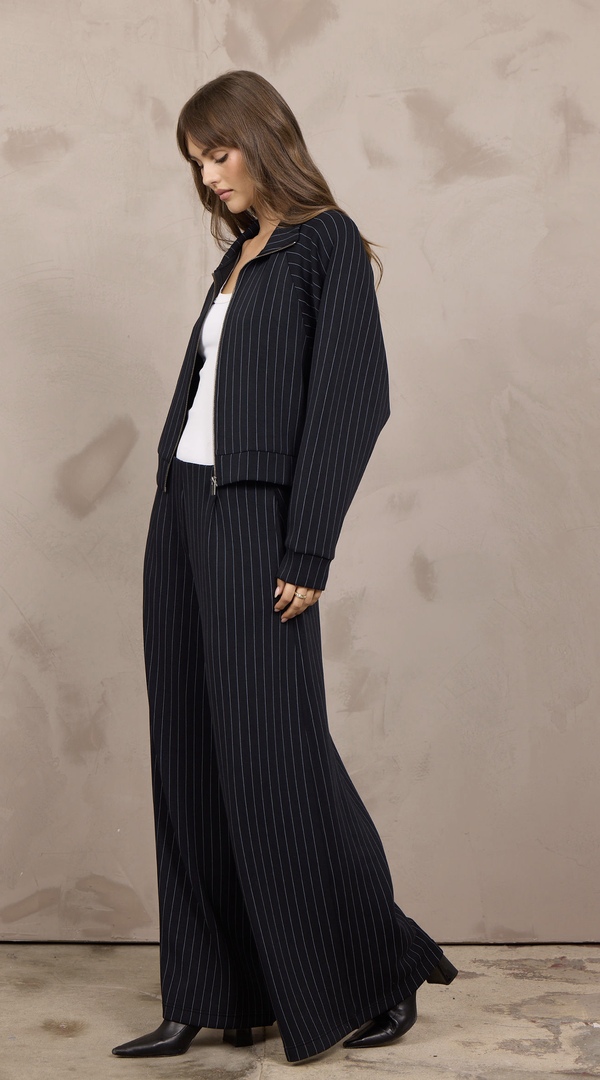 Woman wearing a cropped pinstripe zip-up jacket with a stand collar and ribbed cuffs.