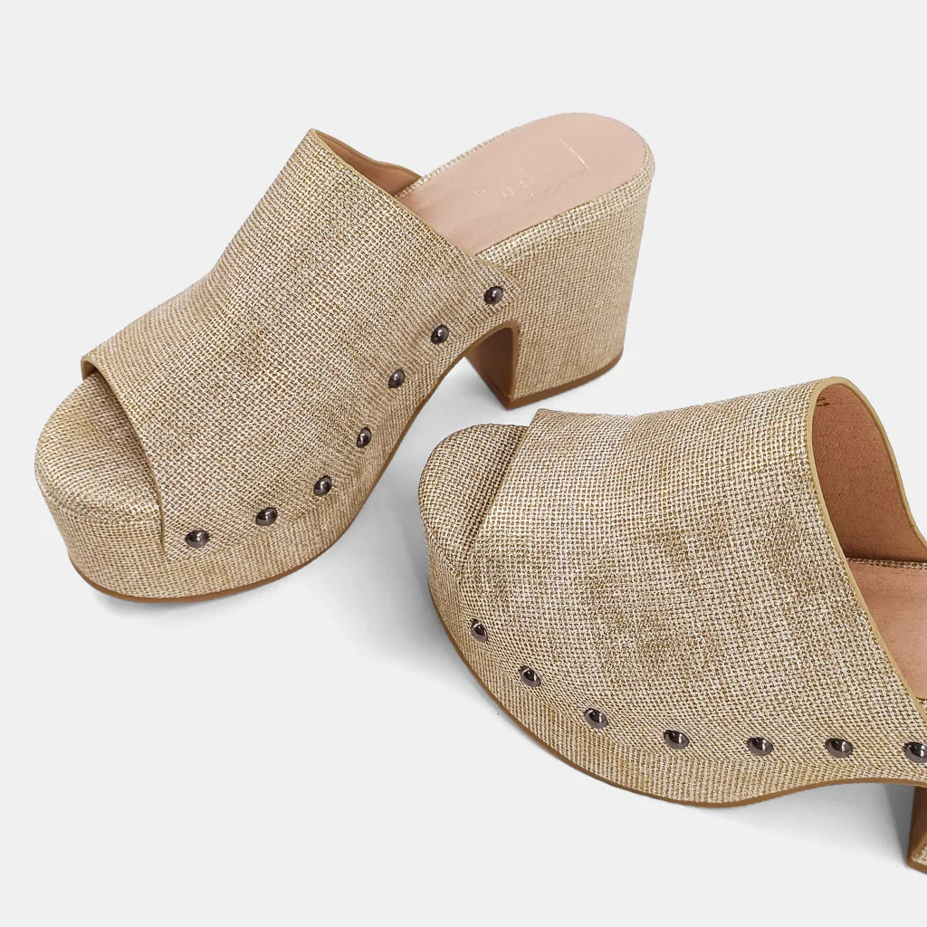 Gina Clog Gold Woven. These shoes are crafted from a soft textured faux leather upper, ensuring you look stylish while staying comfortable all day long. Embellished with charming metallic studs that add a touch of glamour to any outfit, these wedges are perfect to take your look from casual to elegant.
