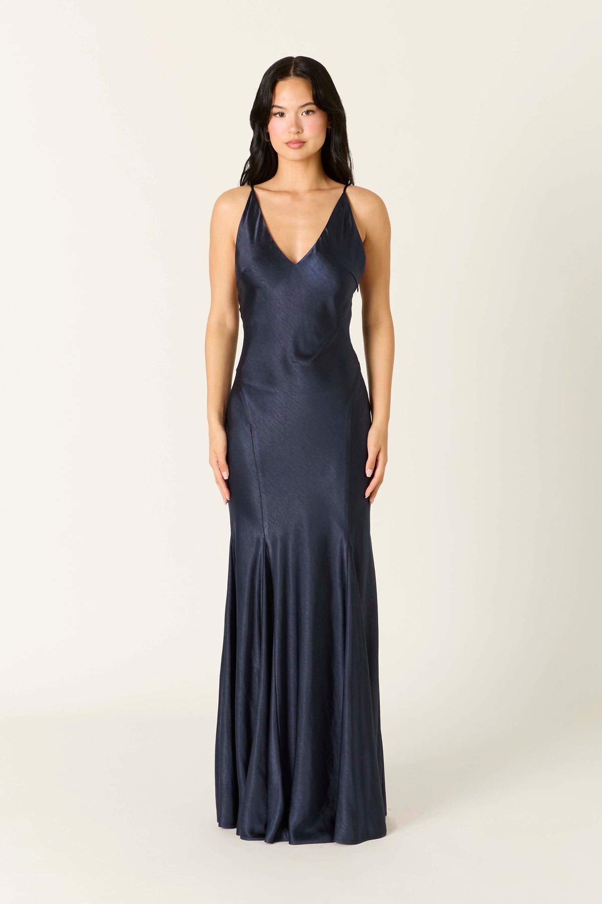 Model wearing a satin maxi slip dress with a V-neckline, thin adjustable straps, low V-back, and flowing flared hem.