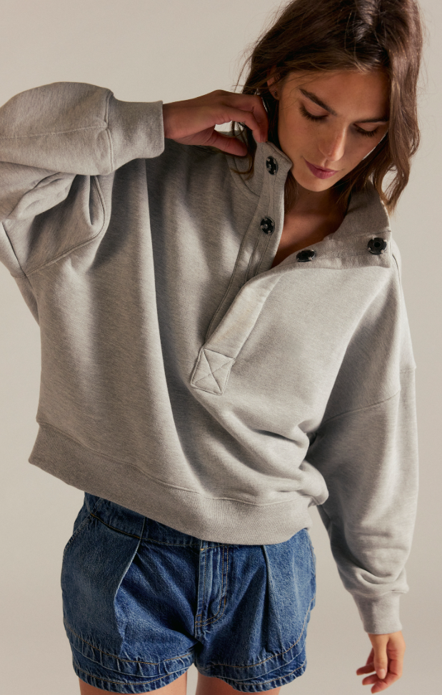 Model wearing an oversized fleece snap-neck pullover sweatshirt with a relaxed fit and long sleeves paired with denim shorts.