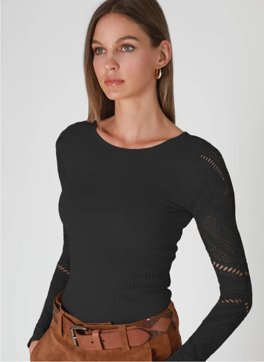 A woman modeling a black long-sleeve knit top with openwork cutout details on the sleeves, paired with brown pants and a belt, against a light gray studio background. A small label in the bottom right reads '6 BLACK'.