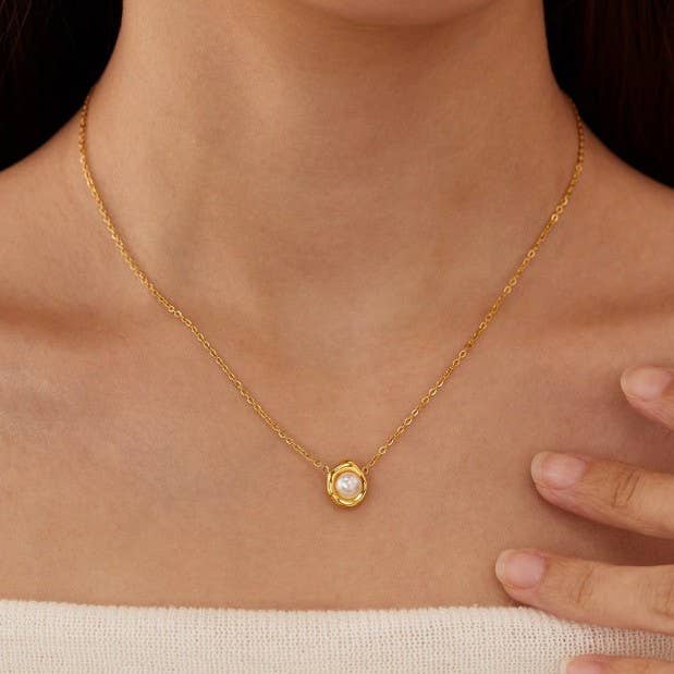 Delicate gold-tone chain necklace featuring a round pearl-inspired pendant in a bezel setting, worn on a model with a strapless knit top.