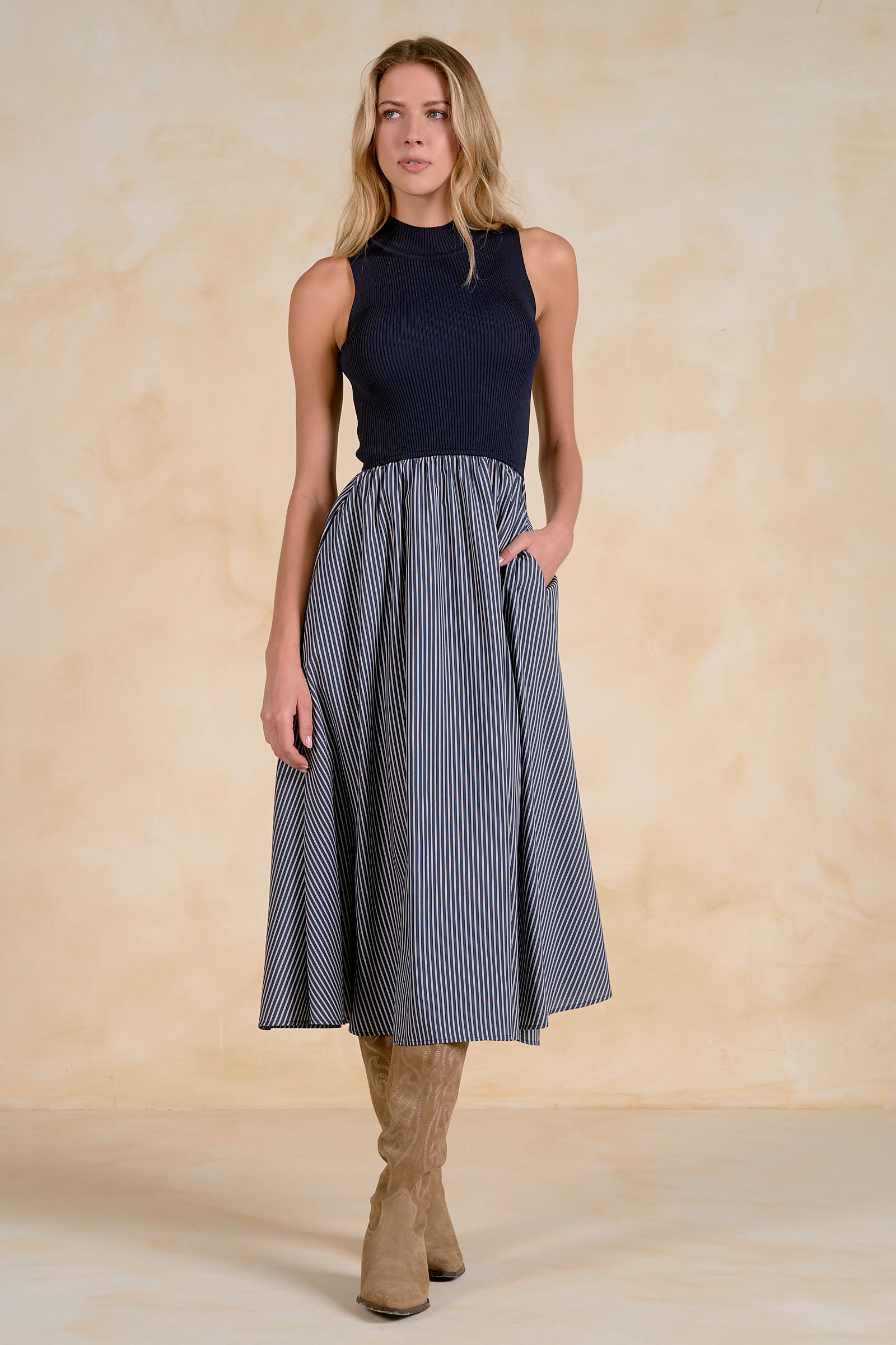 Model wearing a sleeveless midi dress with a ribbed knit bodice, striped full skirt, and side pockets.