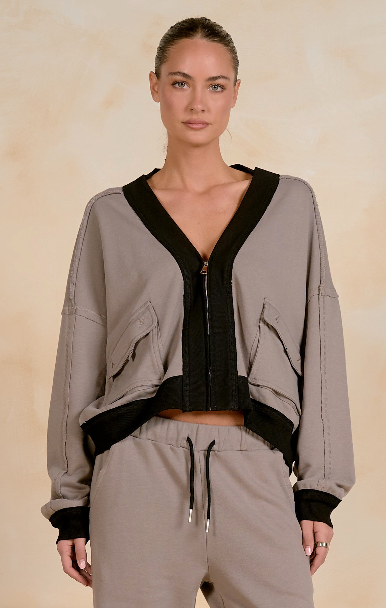 Model wearing a cropped zip-up jacket with contrast trim, utility-inspired flap pockets, and a relaxed fit, styled with matching drawstring joggers against a neutral studio background.
