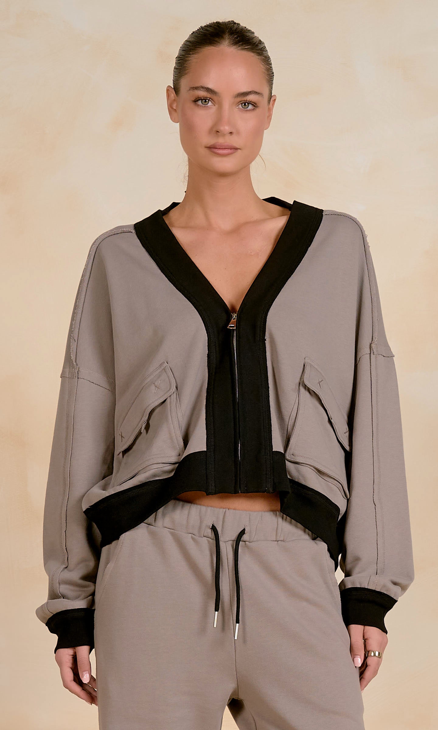 Model wearing a cropped zip-up jacket with contrast trim, utility-inspired flap pockets, and a relaxed fit, styled with matching drawstring joggers against a neutral studio background.