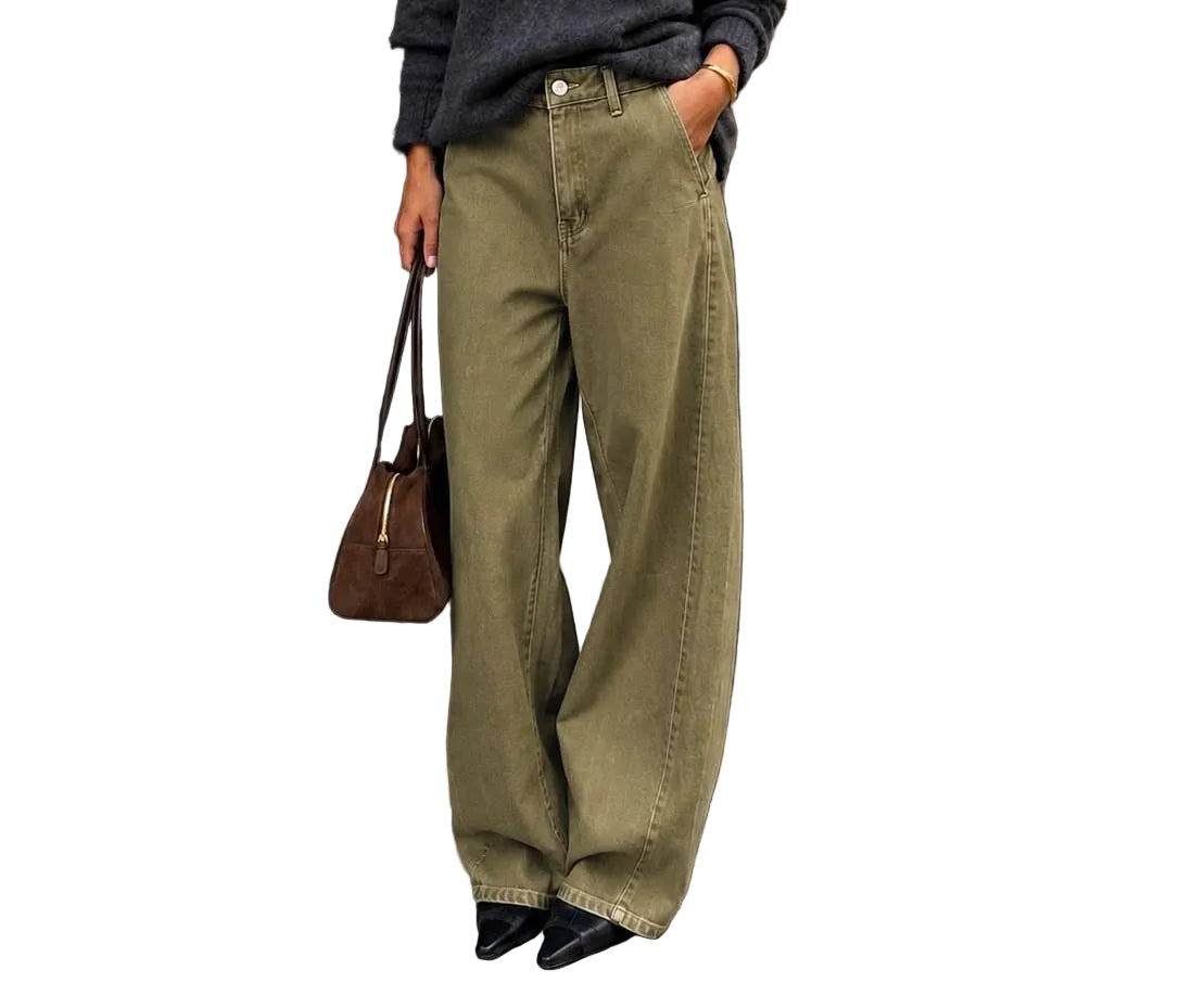 A woman stands on a city sidewalk wearing a dark charcoal knit sweater, olive green wide-leg jeans, black pointed shoes, and sunglasses, holding a brown handbag.