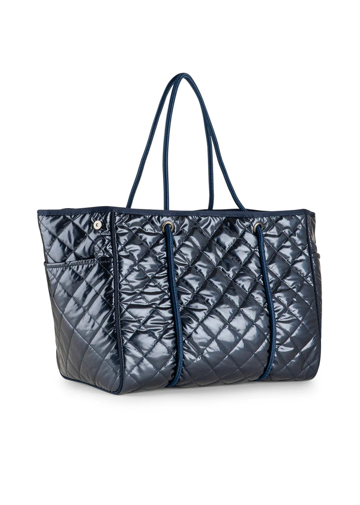 Haute Shore Greyson Navy Shiny Quilted Puffer. This shiny navy puffer tote is the perfect chic everyday bag to use as a carry all for your must haves, with a lightweight design that's perfect for when you're on the go.