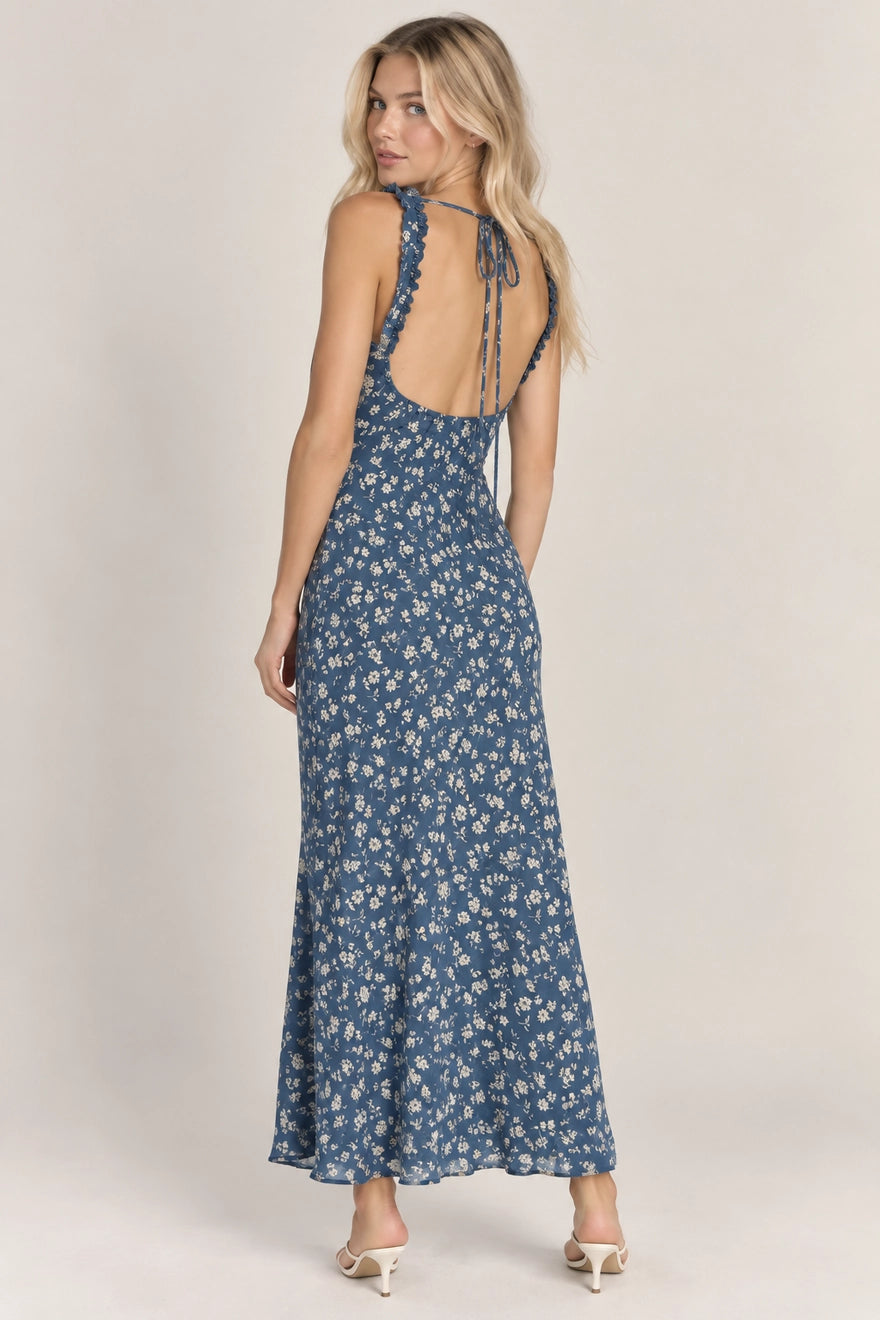 A woman modeling a sleeveless, open-back maxi dress with a blue and white floral pattern, photographed against a plain light beige studio background.