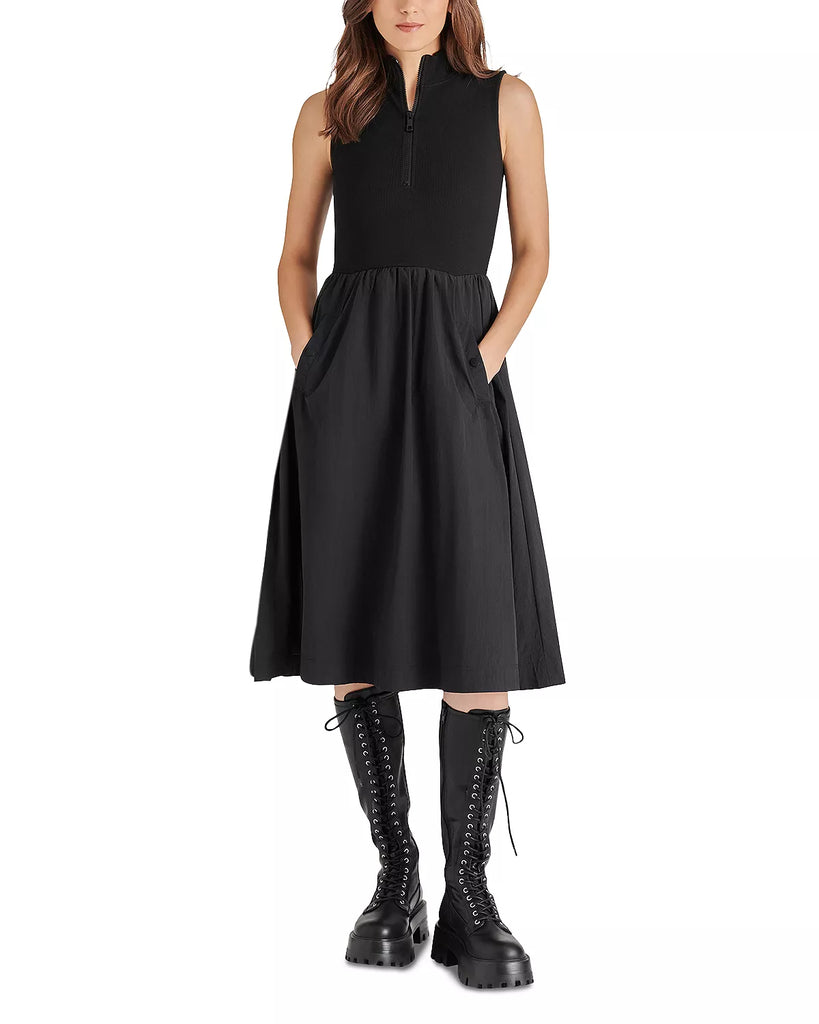 Steve Madden Berlin Dress Black. This dress is s a versatile and chic addition to any wardrobe. With a stylish combination of a sleeveless knit top and a nylon a-line skirt, this midi length dress is both comfortable and fashionable. Perfect for spring, it features a zip front, mock neck, and snap pockets for added functionality.