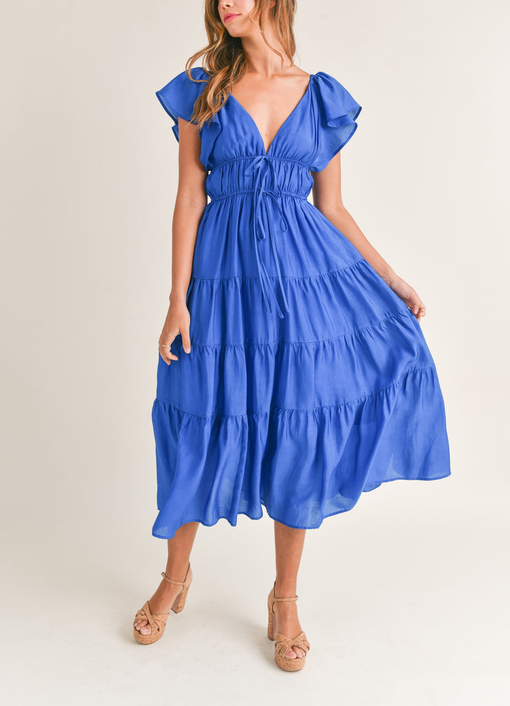 Ingrid Tiered Midi Dress Cobalt Blue. This tiered midi dress features a v-neckline with flutter sleeves and front tie details, the perfect pop of color to stand out this spring and summer, day or night.