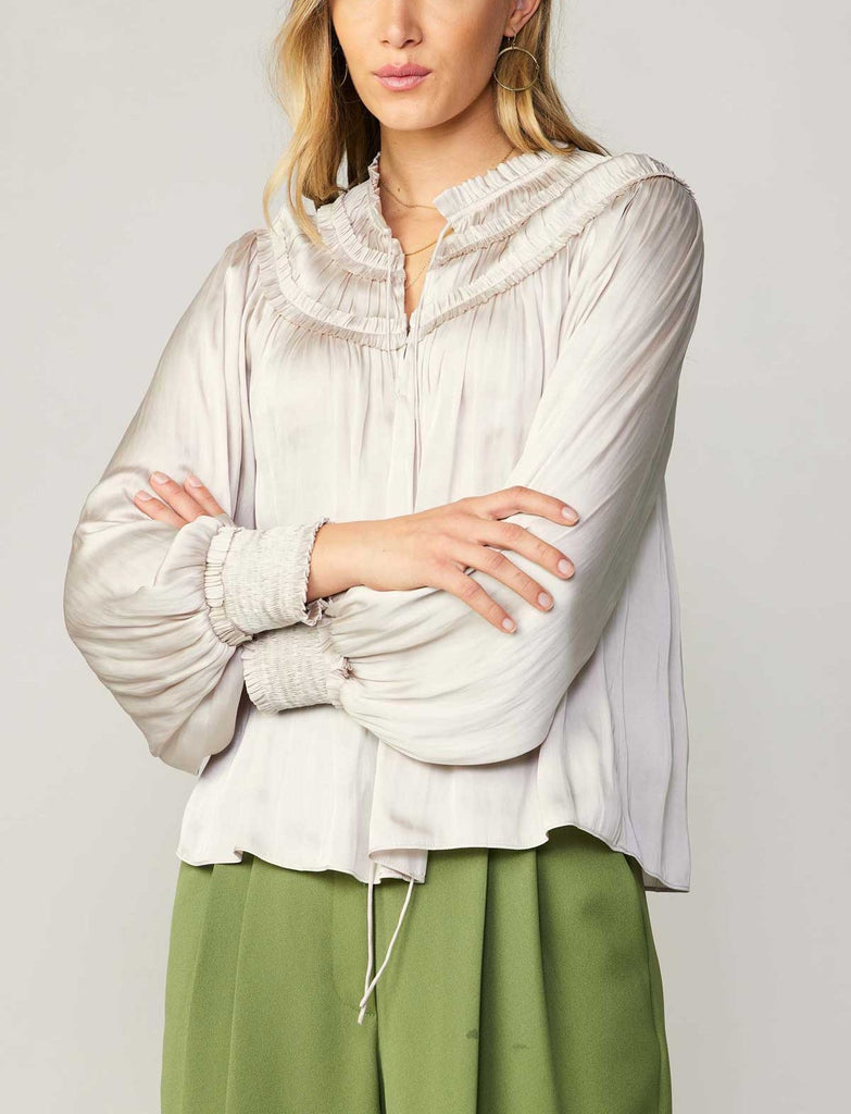 Current Air Ruffle Smock Detail Blouse White. This split-neck blouse exudes an aura of romance in a flowy silhouette with long sleeves and smocked cuffs. Accented by a dainty tied neckline and delicate ruffles at the shoulders, it's a breezy expression of feminine charm.