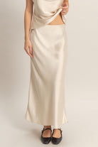 Woman wearing a silky slip midi skirt with a smooth drape and fluid silhouette, styled with a matching top and flats