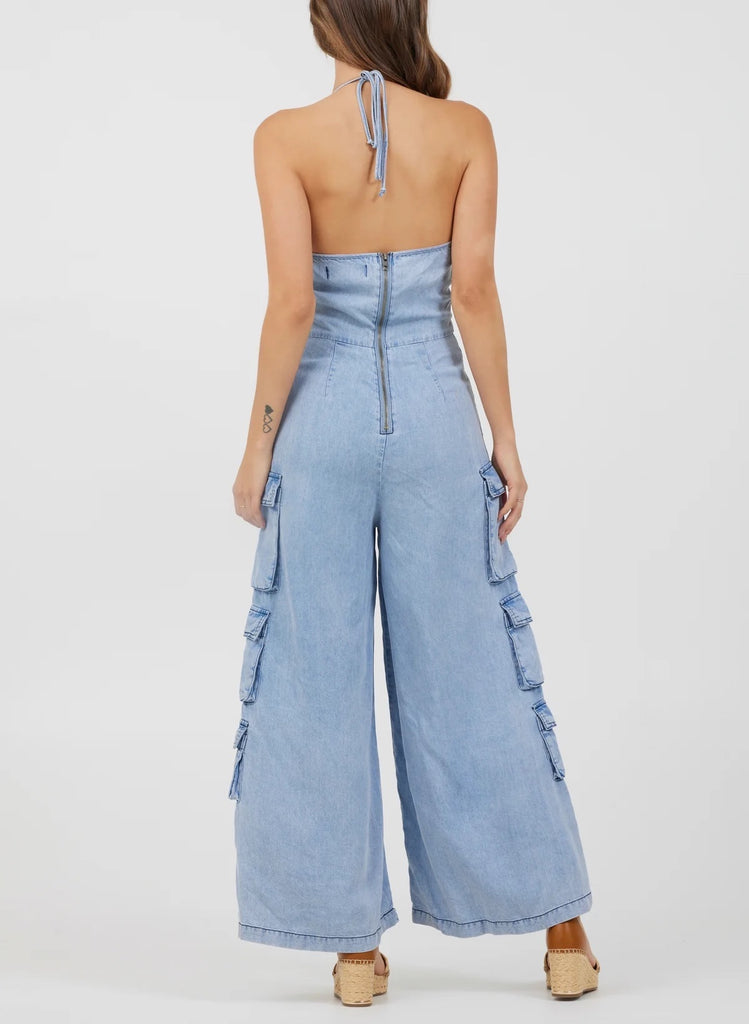 Vintage Havana Tencel Jumpsuit Washed Denim. This adorable tencel jumpsuit features a tie halter neckline with a zip back closure and a wide leg fit with cargo pocket details, the perfect piece to throw on for a quick trendy look.