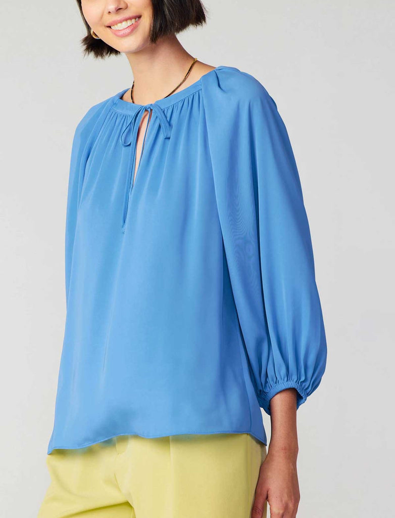 Current Air Pleated Raglan Blouse Azure Blue. This long sleeve split neck top features a self-tie and that can be worn open for a v-neck look, the azure blue color is striking against black or white.