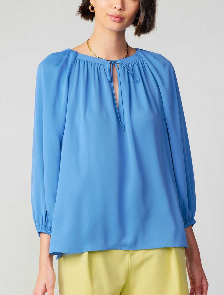 Current Air Pleated Raglan Blouse Azure Blue. This long sleeve split neck top features a self-tie and that can be worn open for a v-neck look, the azure blue color is striking against black or white.