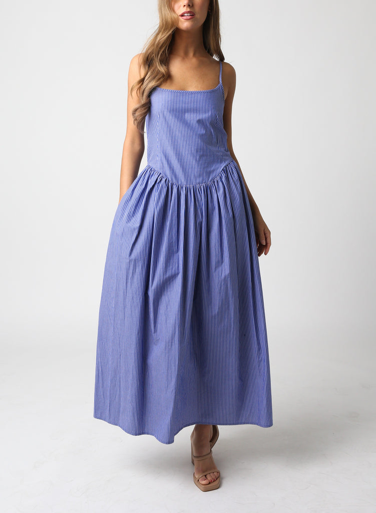 Keiran Stipe Tie Back Maxi Dress Blue Denim. This sleeveless maxi dress features a square neckline with a tie back and stripe pattern throughout, the perfect dress to throw on with heels and a white jacket.