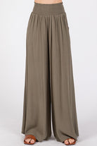 Model wearing flowy wide-leg pants with a smocked waistband, side pockets, and a relaxed fit.