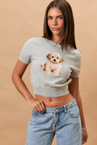 Model wearing a cropped short-sleeve knit sweater featuring a puppy graphic with a crew neckline, styled with relaxed-fit denim.