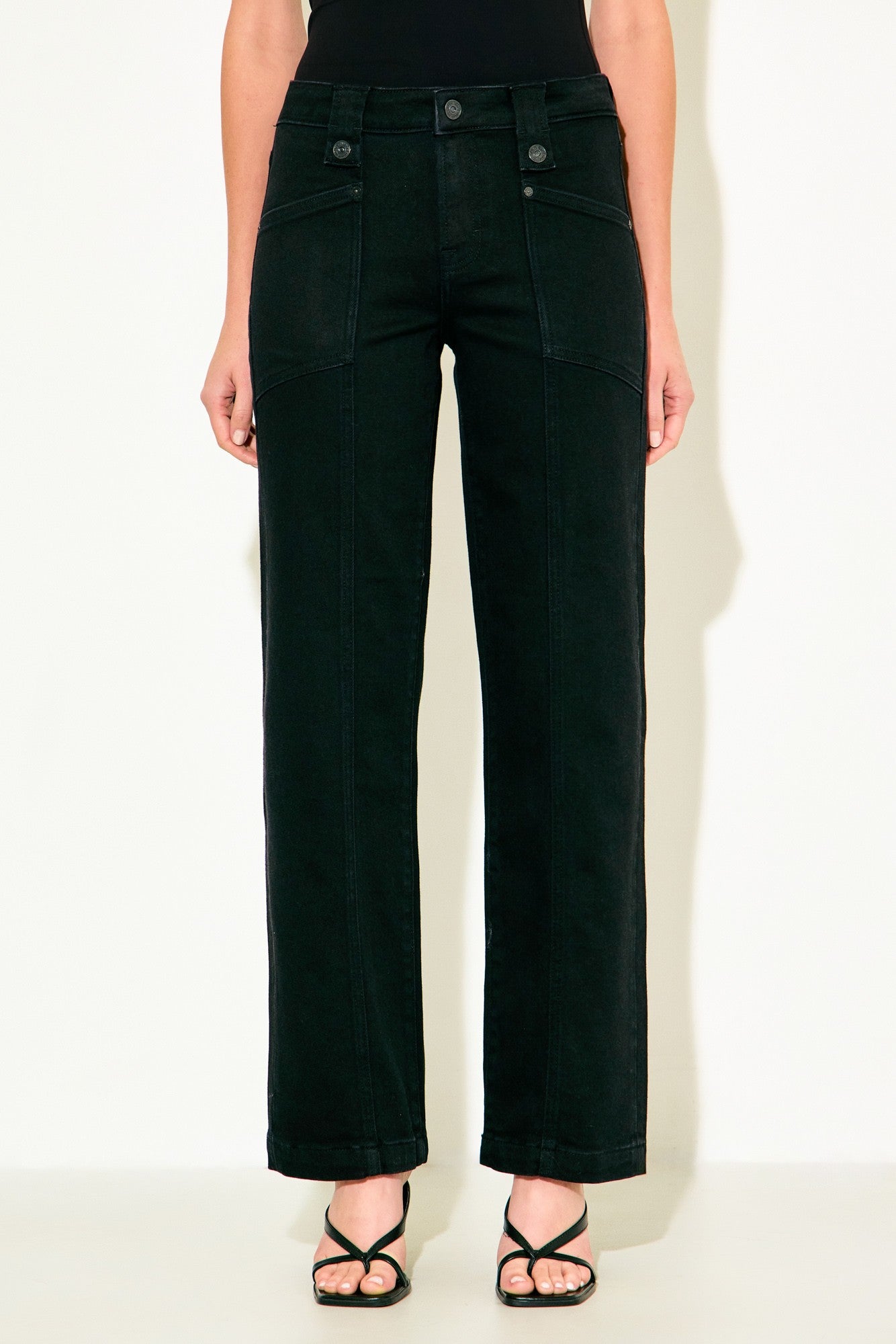A model from the waist down wearing black wide-leg cropped jeans and black strappy sandals, standing against a plain off-white background.
