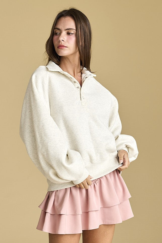 Model wearing an oversized oatmeal half-snap fleece pullover with a relaxed fit styled over a tiered mini skirt.