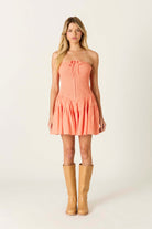 Strapless smocked mini dress with a fitted bodice, front tie detail, and tiered skirt, styled with tall boots