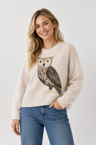 Woman wearing a cream sweater with an owl design on a plain background