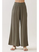 Model wearing flowy wide-leg pants with a smocked waistband, side pockets, and a relaxed wide-leg silhouette.