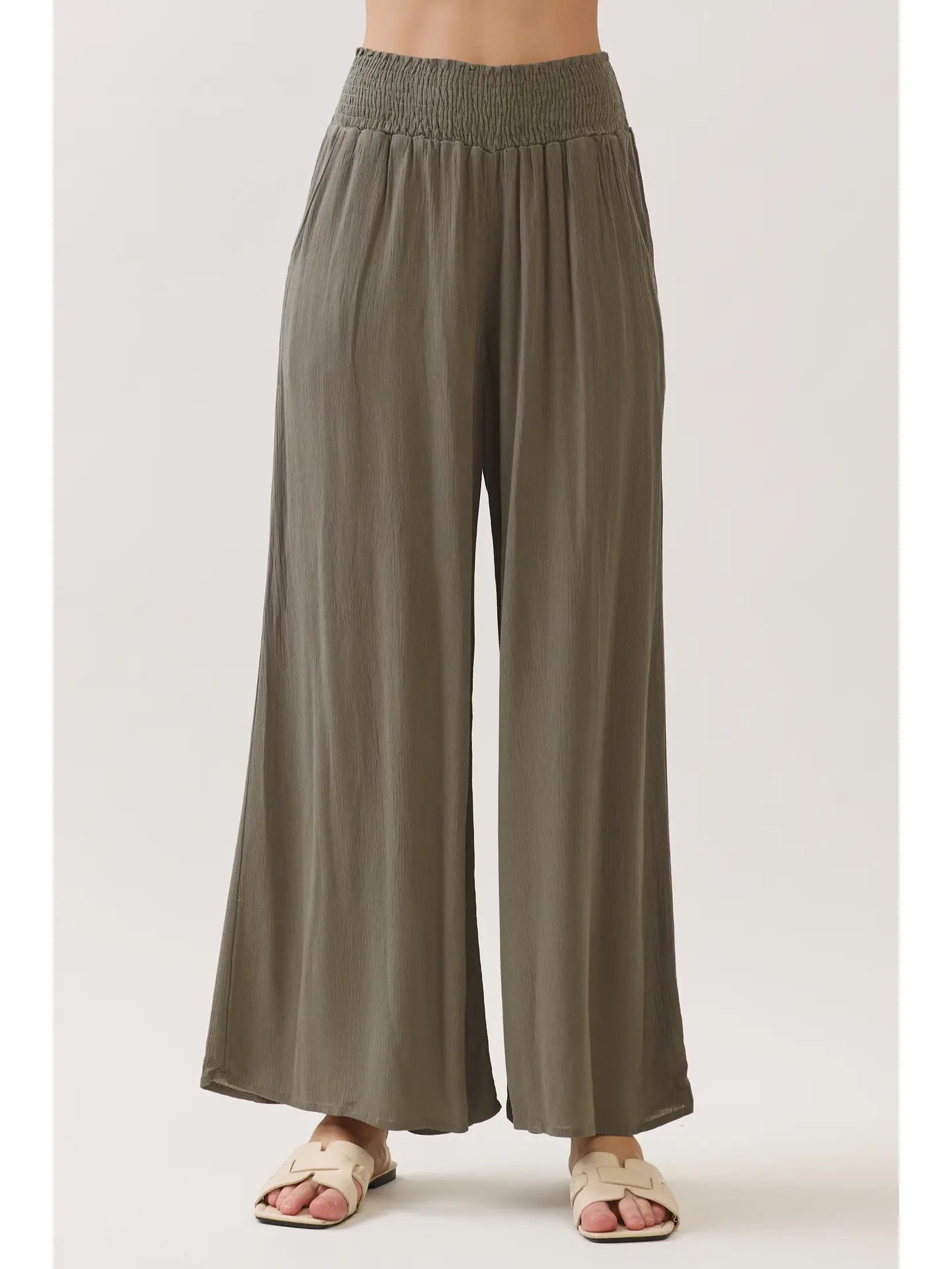 Model wearing flowy wide-leg pants with a smocked waistband, side pockets, and a relaxed wide-leg silhouette.