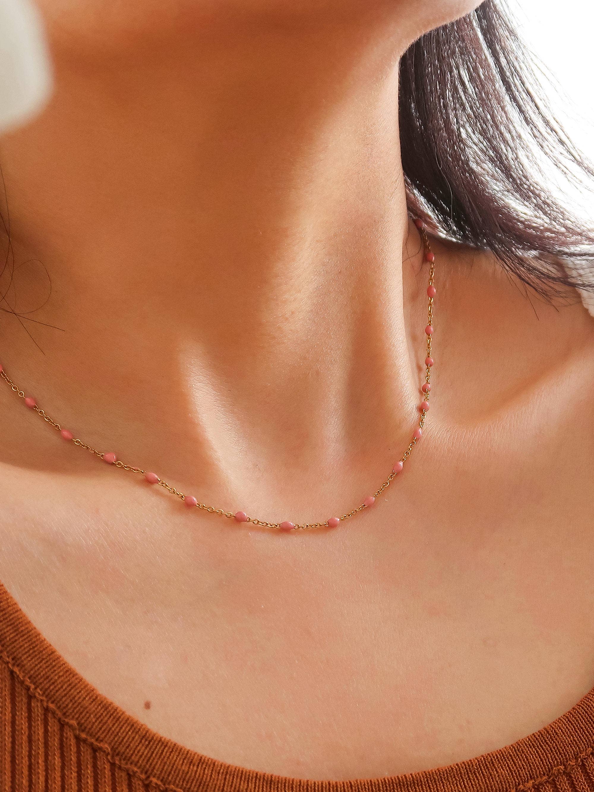 Dainty gold-tone chain necklace featuring evenly spaced pink bead accents, styled as a delicate layering necklace with a minimalist design.