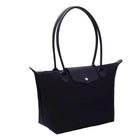 A black tote bag with double top handles and a front flap pocket, styled on a white surface next to stacked books against a white curtain backdrop.