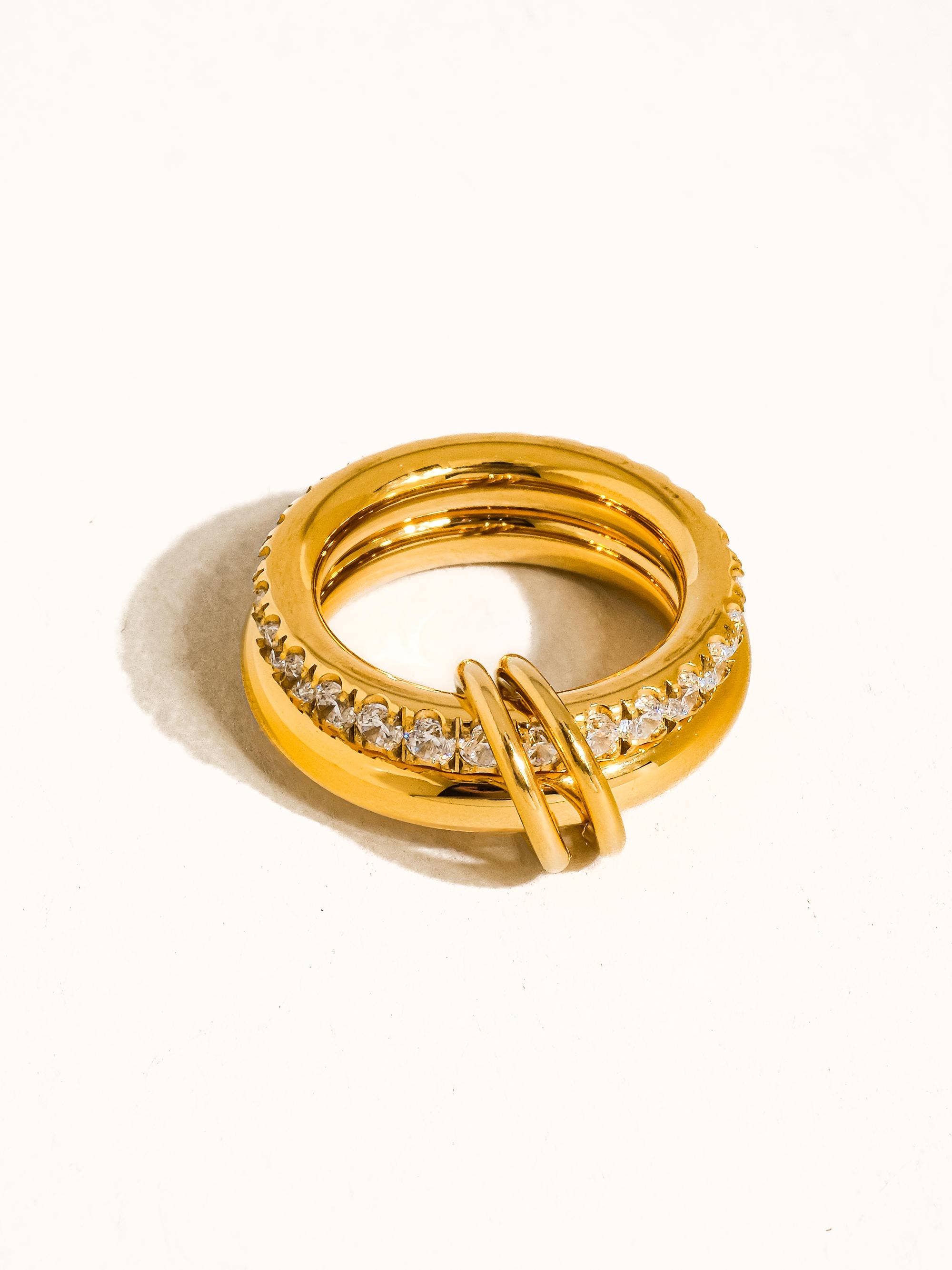 Chunky gold statement ring with pavé crystal detailing and interlocking accent on a neutral background.
