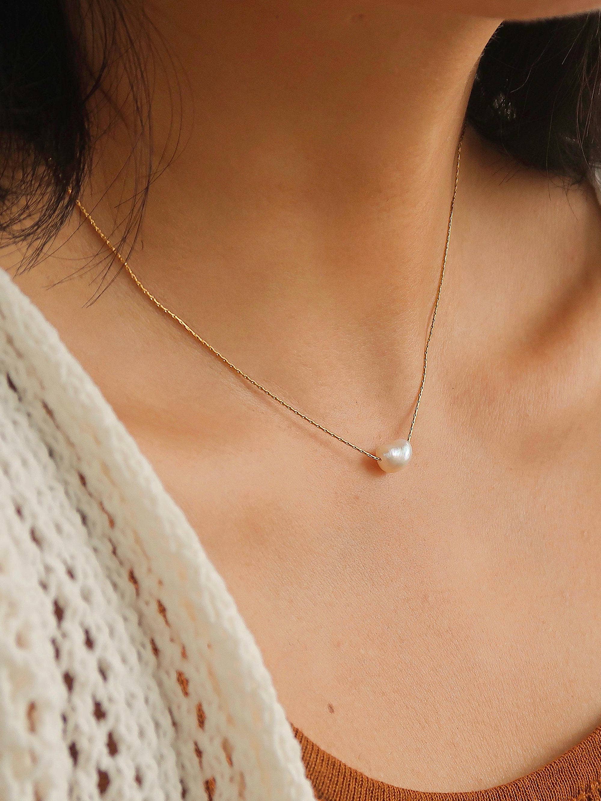 Delicate gold-tone chain necklace featuring a single freshwater pearl pendant, styled as a minimalist everyday accessory.