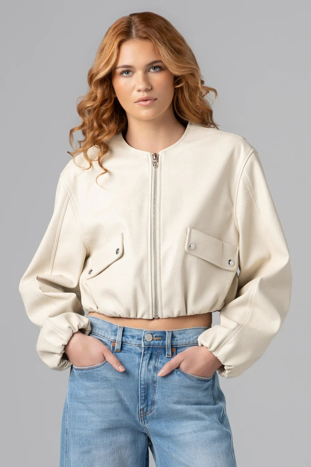 Woman wearing a cropped zip front jacket with utility pocket details and long sleeves styled with denim jeans