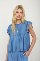 Sleeveless pleated blouse with tie-front detail and relaxed fit worn with denim jeans