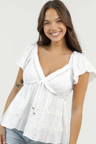 Eyelet blouse with v-neckline, flutter sleeves, and tiered silhouette styled with denim