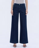 Model wearing high-rise dark wash wide-leg jeans with a clean finish, styled with a fitted neutral bodysuit and sandals against a white studio background.