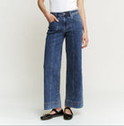 A woman modeling a white short-sleeve crewneck top and high-waisted, wide-leg blue denim jeans with black flat shoes, standing against a plain light gray studio background.