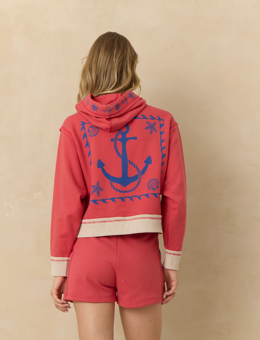 Cropped coral hoodie with nautical anchor graphic on the back, contrast trim, quarter zip neckline, and relaxed fit paired with matching lounge shorts.