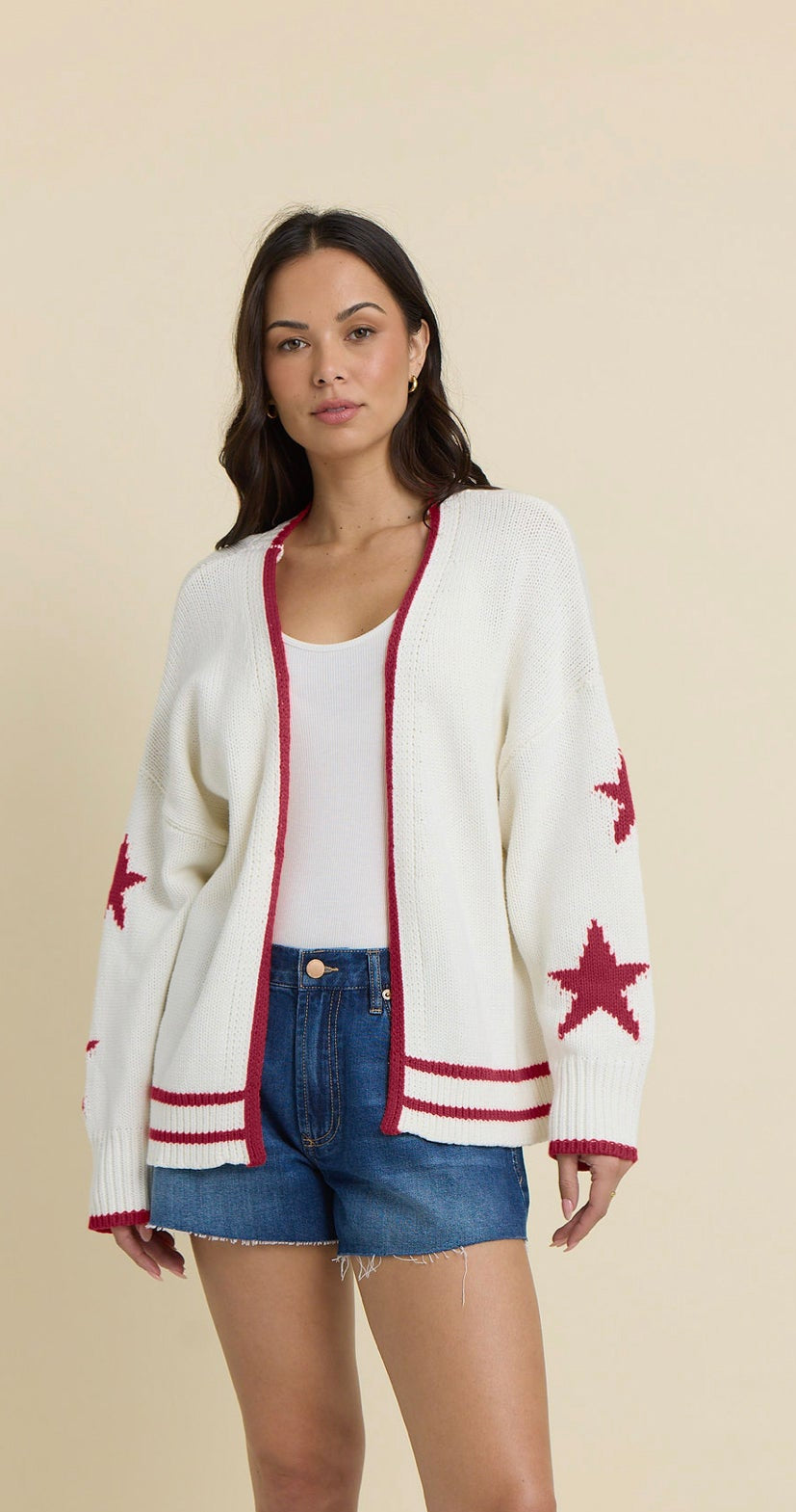 Cream knit cardigan with red star sleeve details, contrast trim, and American flag graphic on the back paired with denim shorts.