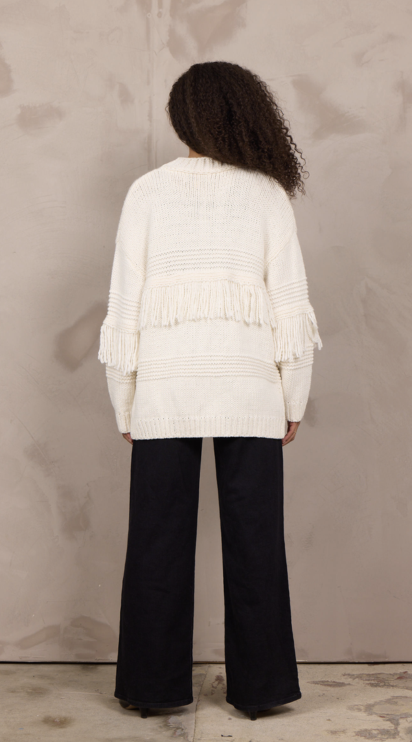 Woman wearing an oversized open-front cable knit cardigan with fringe trim and ribbed cuffs.