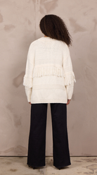 Woman wearing an oversized open-front cable knit cardigan with fringe trim and ribbed cuffs.