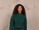 Woman wearing a mockneck pullover with contrast stitching.