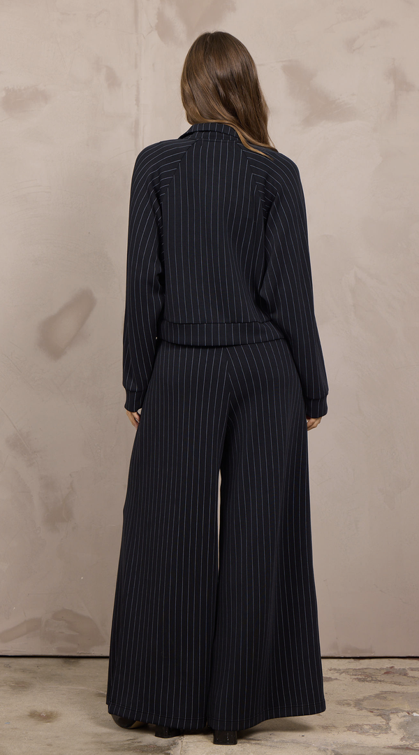 Woman wearing a cropped pinstripe zip-up jacket with a stand collar and ribbed cuffs.