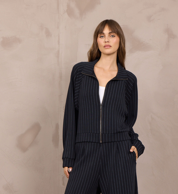 Woman wearing a cropped pinstripe zip-up jacket with a stand collar and ribbed cuffs.